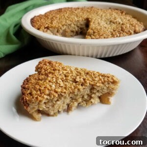 A neatly served slice of apple pie baked oatmeal on a plate, with the remainder of the wholesome dish visible in a pie plate in the background.