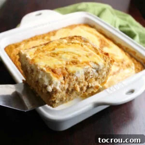 The first delicious piece of pumpkin roll baked oatmeal, showing off its creamy swirl, being carefully lifted from the pan.