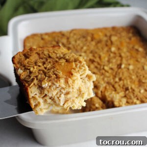 A delectable piece of peach baked oatmeal being lifted from the pan, highlighting its juicy peach chunks and soft texture.