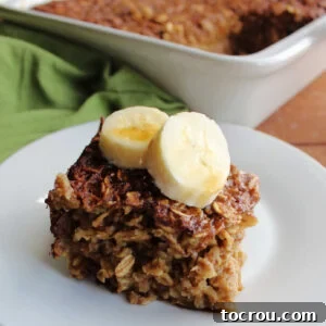 A generous slice of soft baked oatmeal, elegantly topped with fresh banana slices and a luscious drizzle of maple syrup.