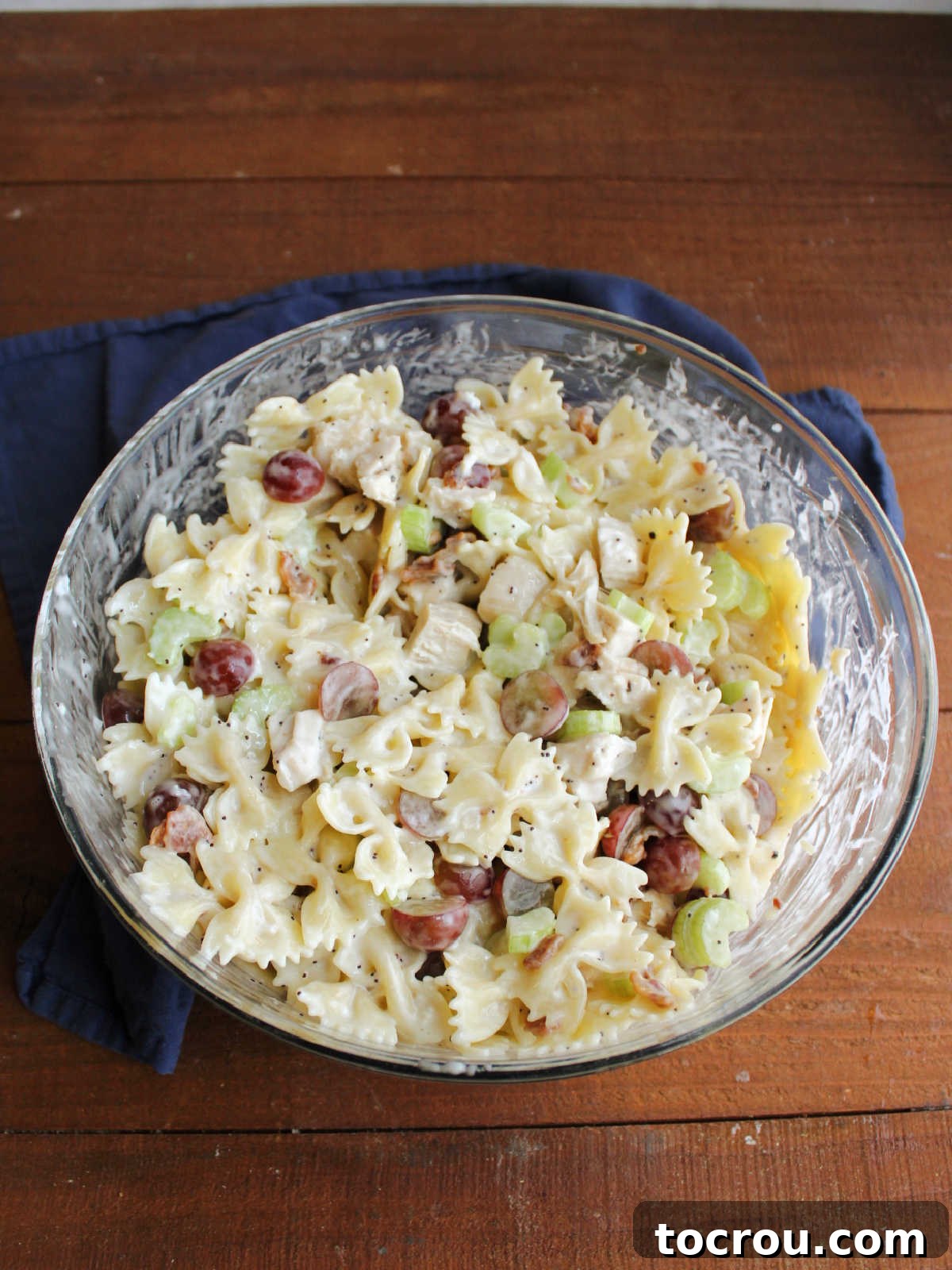 Refreshing Poppy Seed Chicken Pasta Salad 4 A large glass mixing bowl filled with freshly mixed Chicken Poppy Seed Pasta Salad, showcasing the pasta, dressing, grapes, and celery, ready for chilling.