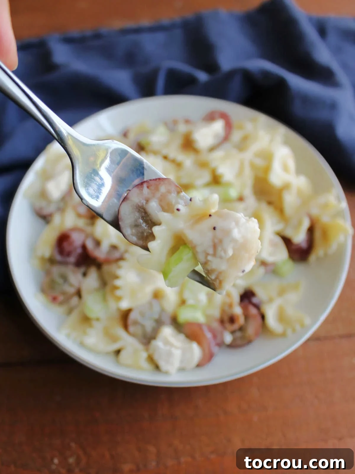 Refreshing Poppy Seed Chicken Pasta Salad 5 A forkful of Chicken Poppy Seed Pasta Salad, featuring a red grape, a piece of chicken, and a sliver of celery, ready to be enjoyed.