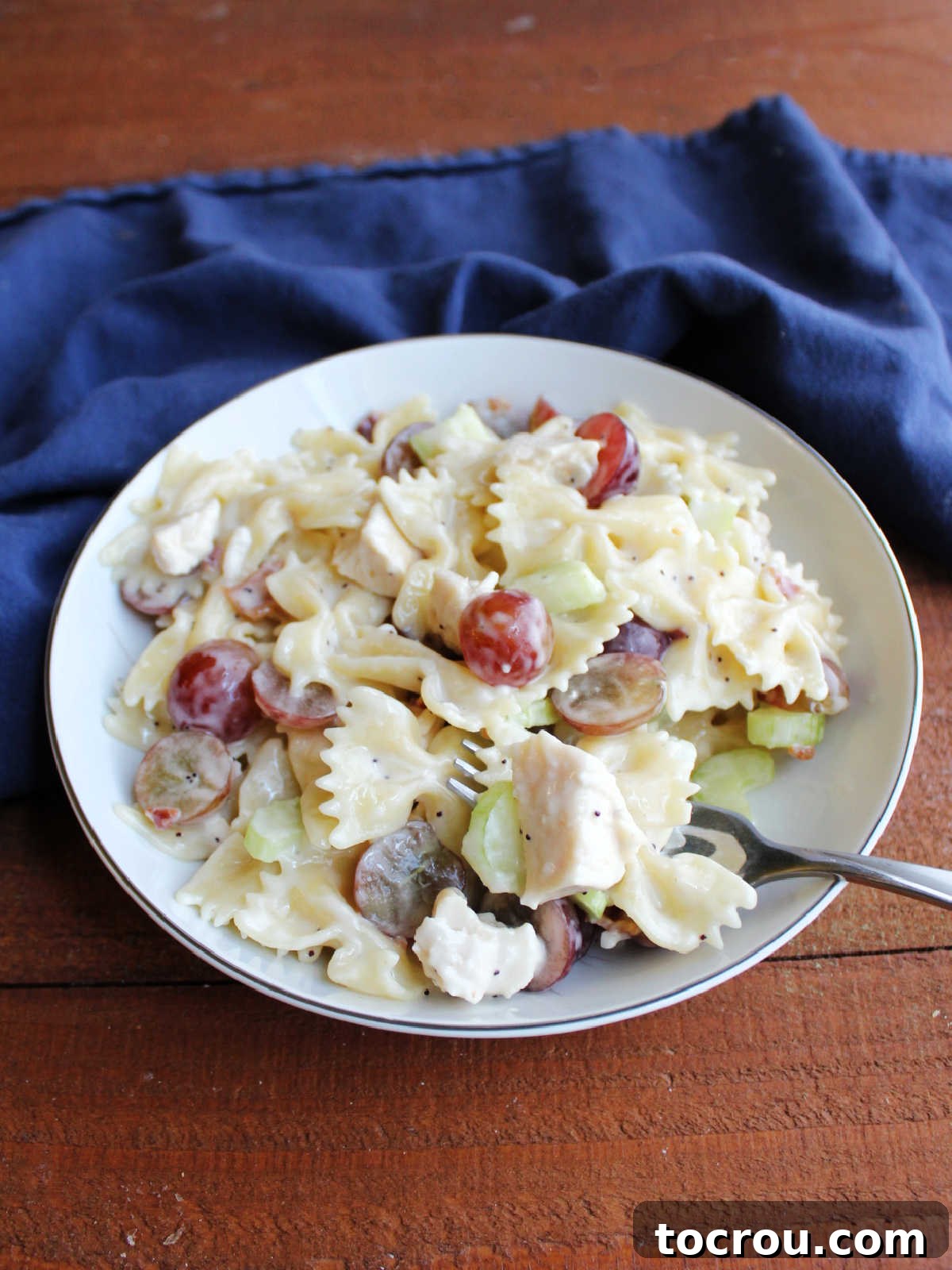 Refreshing Poppy Seed Chicken Pasta Salad 6 A inviting bowl of chicken poppy seed macaroni salad, garnished with vibrant red grapes, crispy bacon bits, and finely chopped celery.