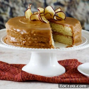 Southern caramel cake with homemade caramel icing topped with apple chips on a white cake pedestal.