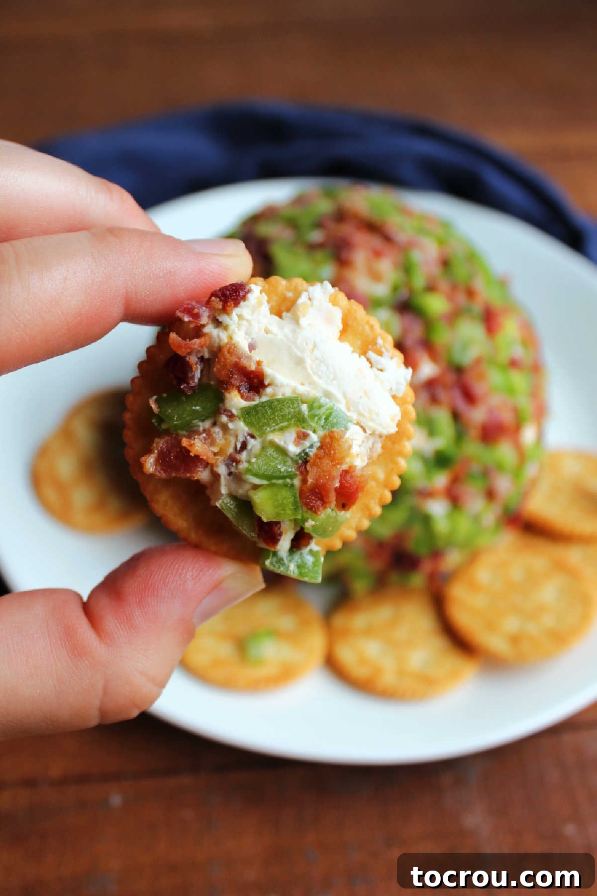 Zingy Bacon Jalapeno Cheese Ball 3 Hand holding cracker with bacon jalapeno cheese ball spread over the top.