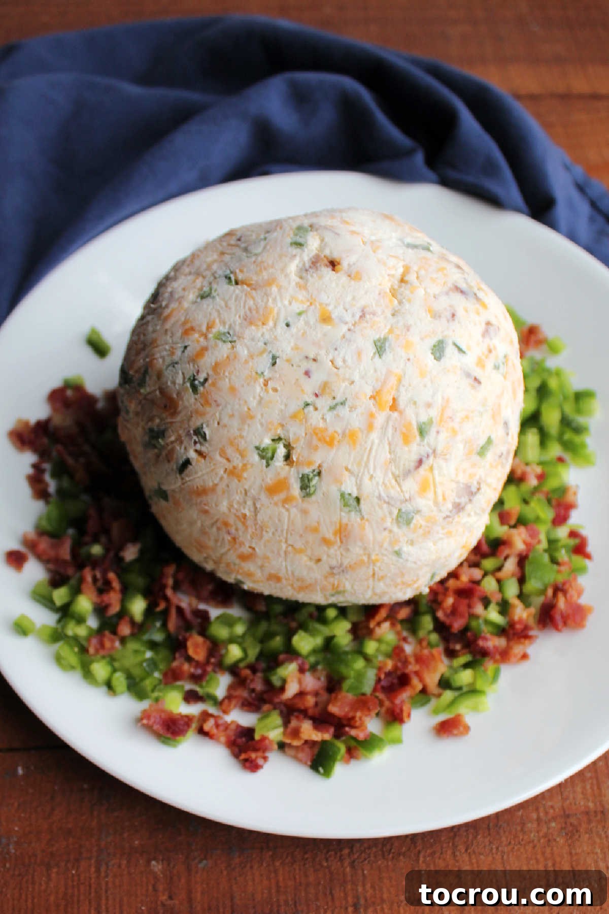 Zingy Bacon Jalapeno Cheese Ball 8 Chilled cheese ball on plate with diced jalapenos and crumbled bacon, ready to be coated and served.