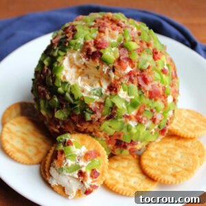 Cheese ball coated in bits of jalapeno pepper and bacon with a little bit missing showing cheesy inside on plate with crackers, ready to eat.