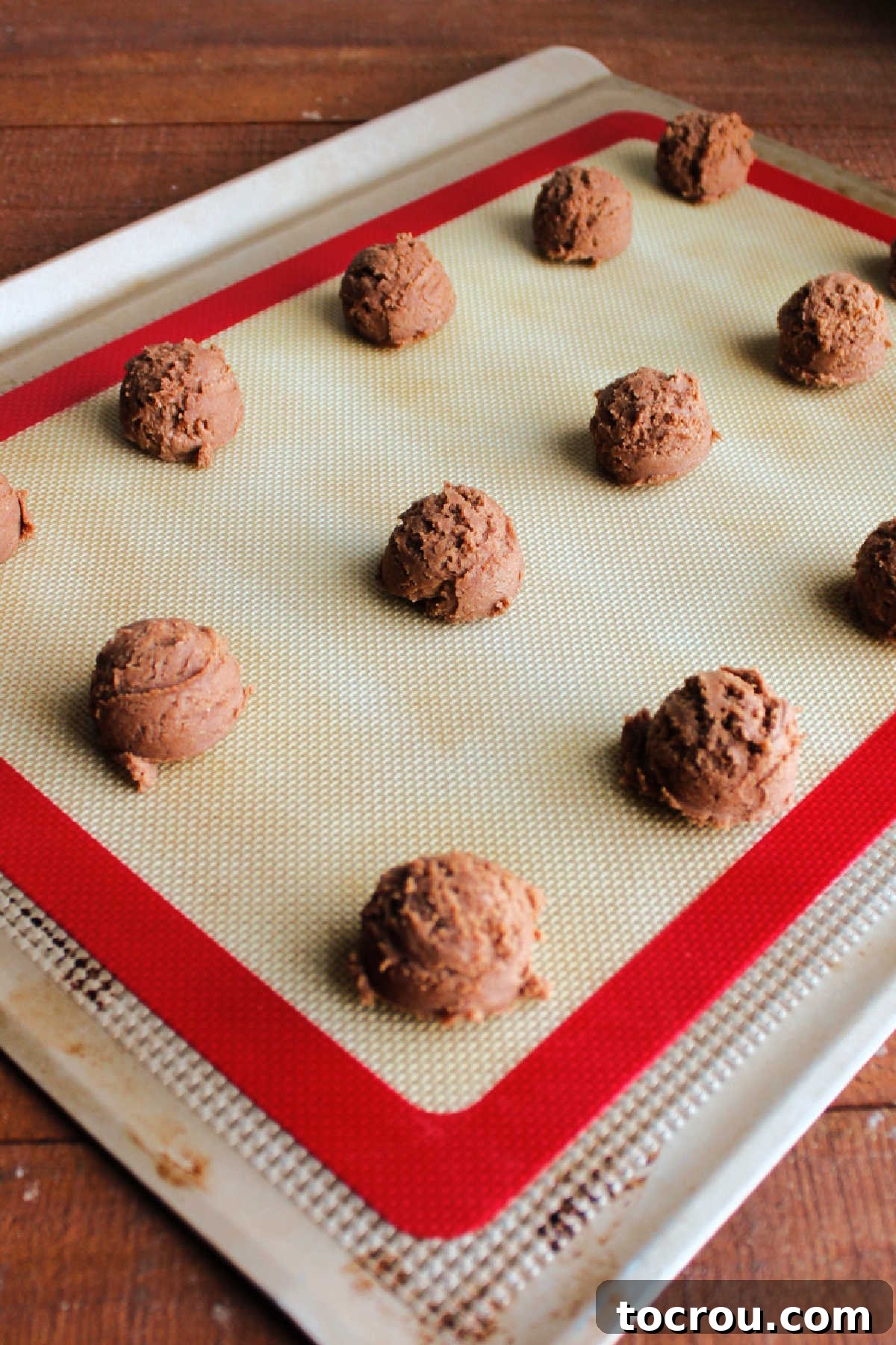 Neatly scooped balls of chocolate cookie dough placed on a silicone mat lined cookie sheet, ready for chilling.