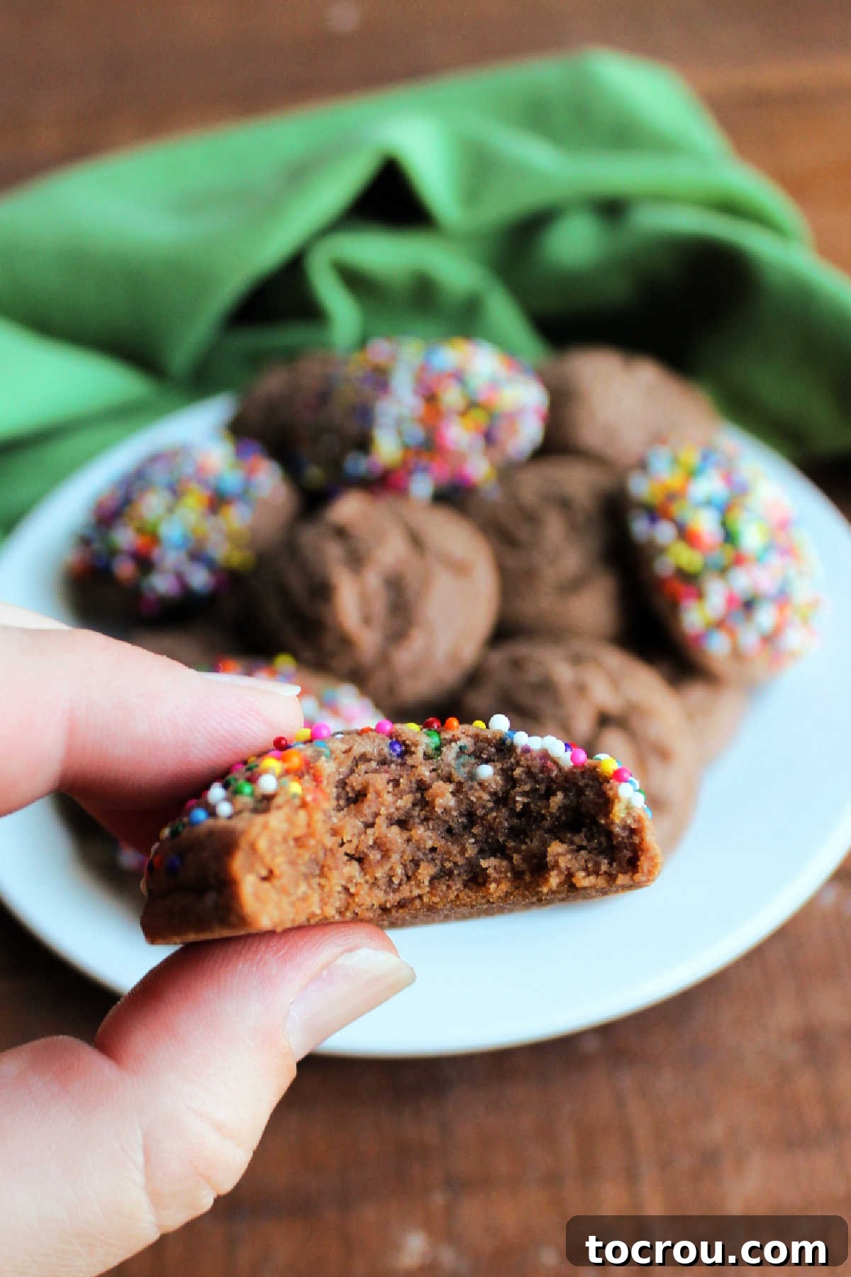 A hand holding a chocolate condensed milk cookie with a bite taken out, revealing its soft and moist interior.