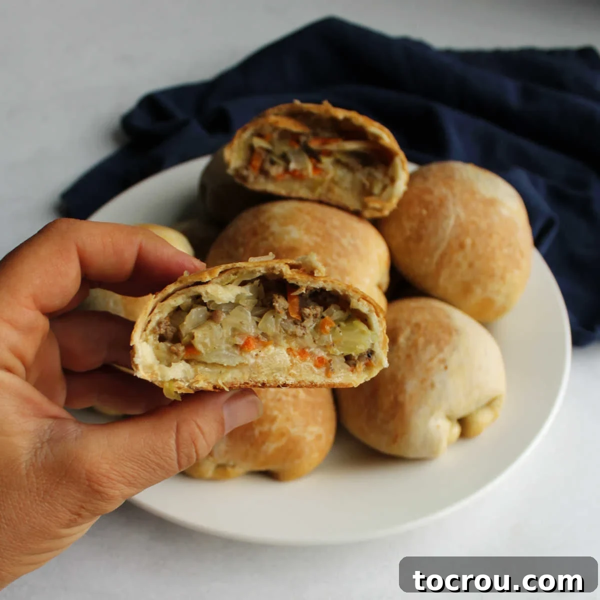 close up of hand holding half of a runza with cabbage and ground beef filling showing.