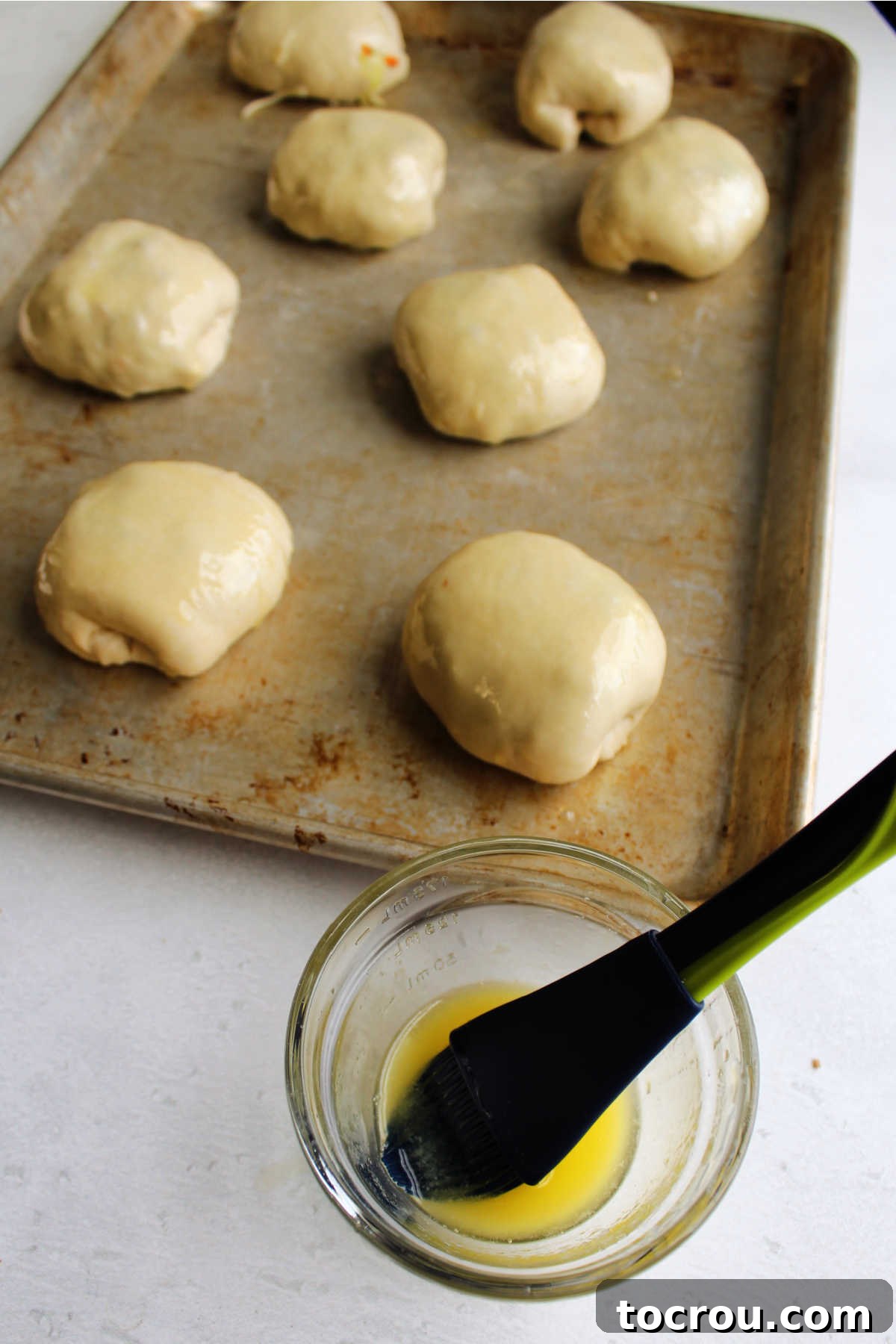 brushing melted butter over stuffed bierock rolls ready to bake.