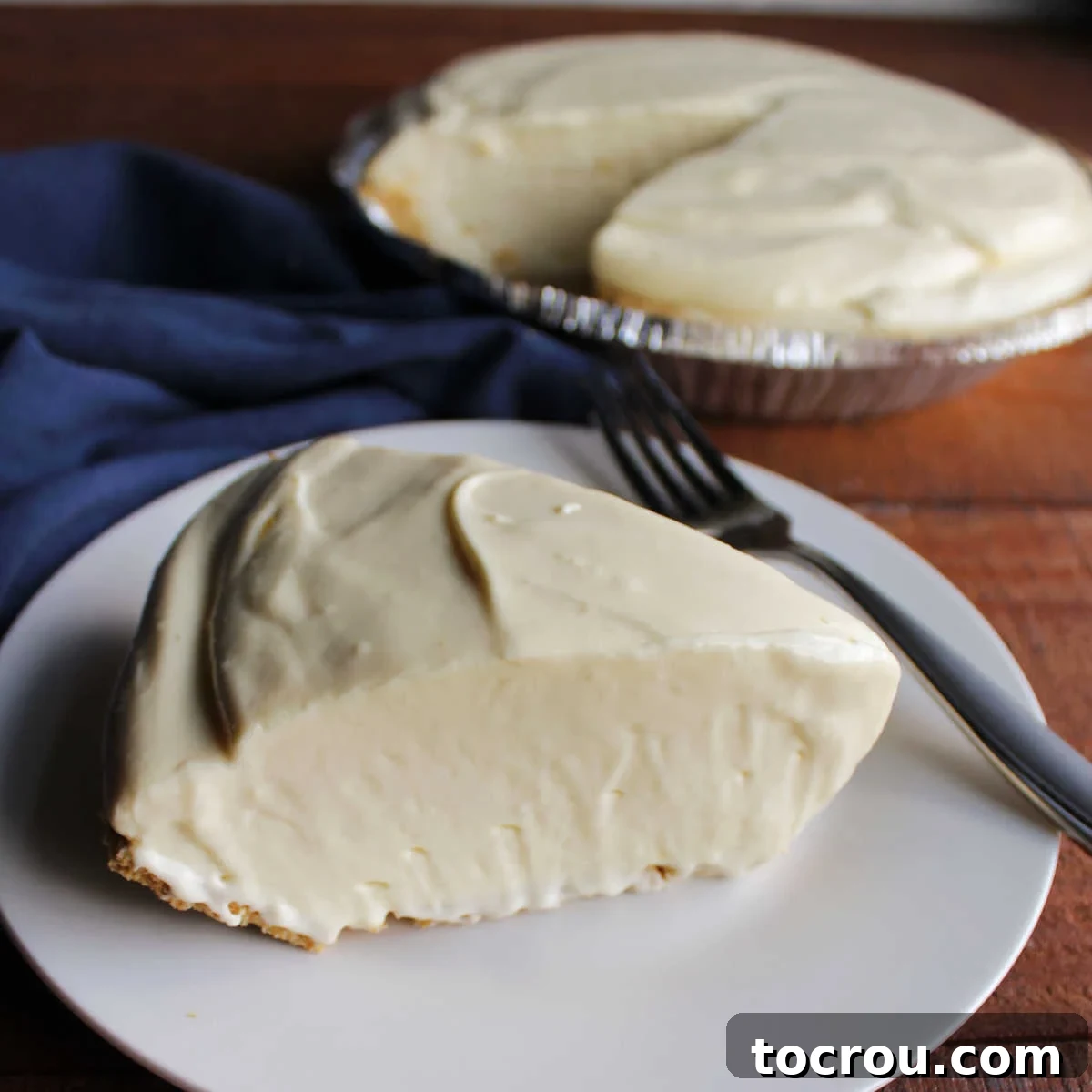 Slice of smooth and creamy orange pie in graham cracker crust with remaining pie in the background. 