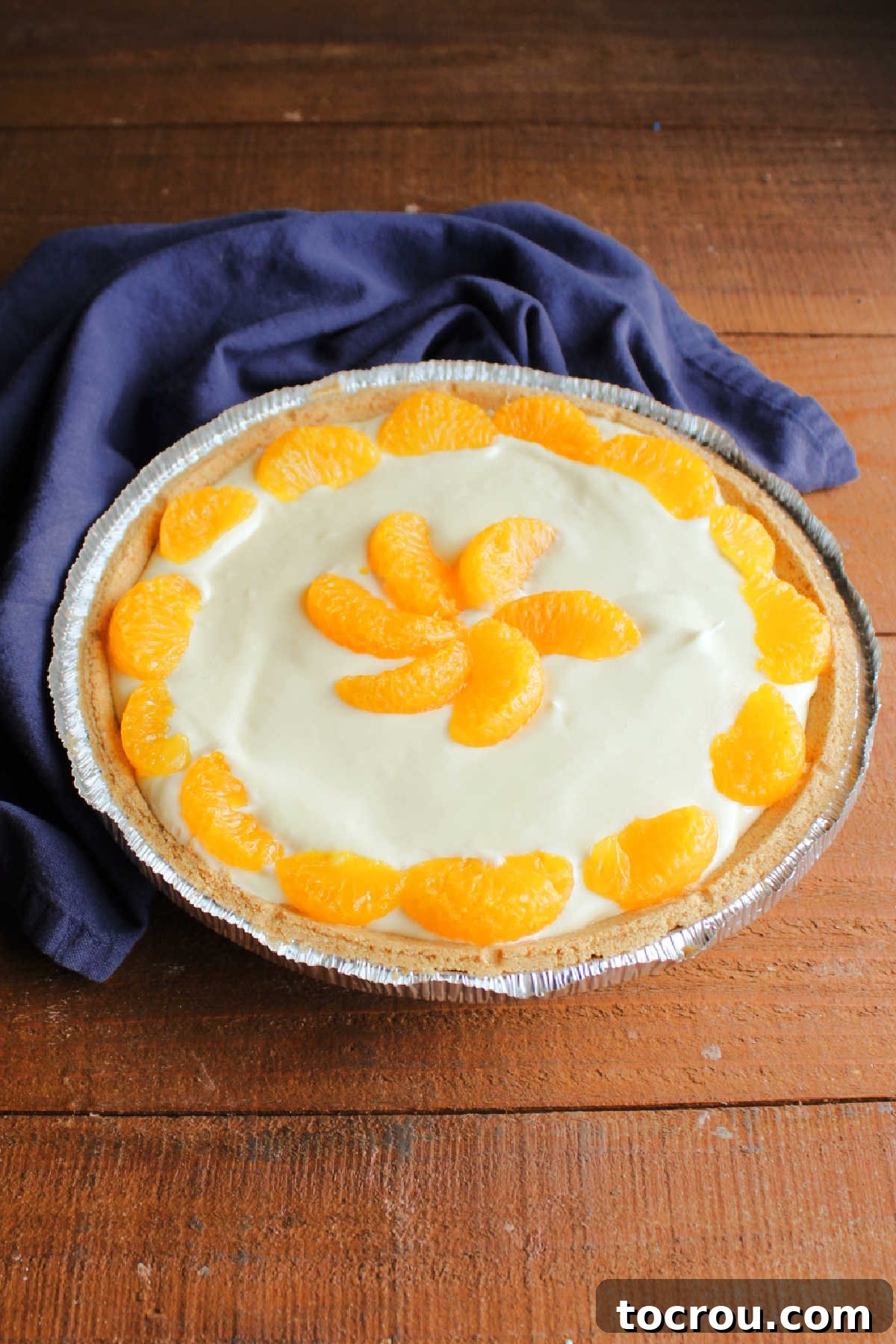 Orange no bake pie with half of the filling in it, garnished with mandarin orange slices.