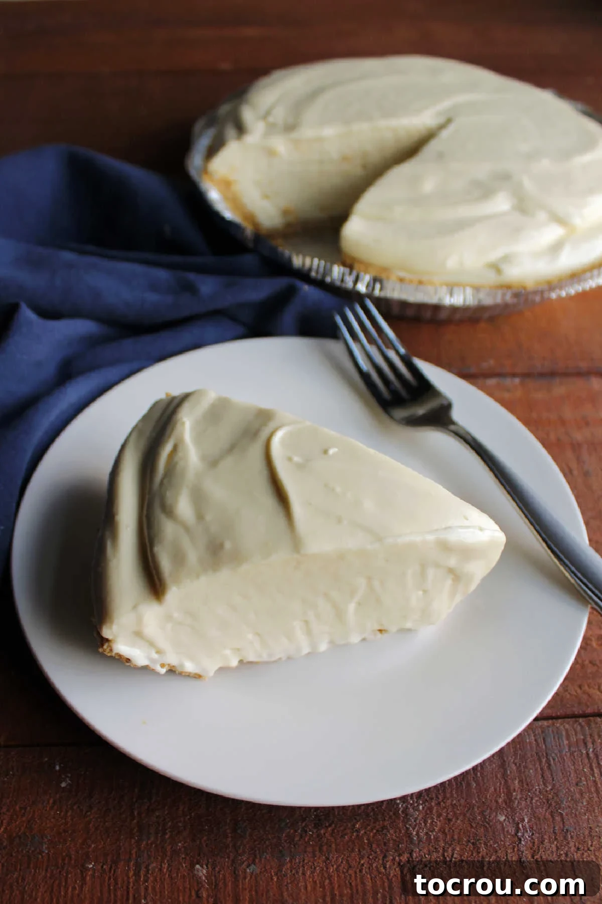 Piece of thick orange cream pie on plate with remaining pie behind it.
