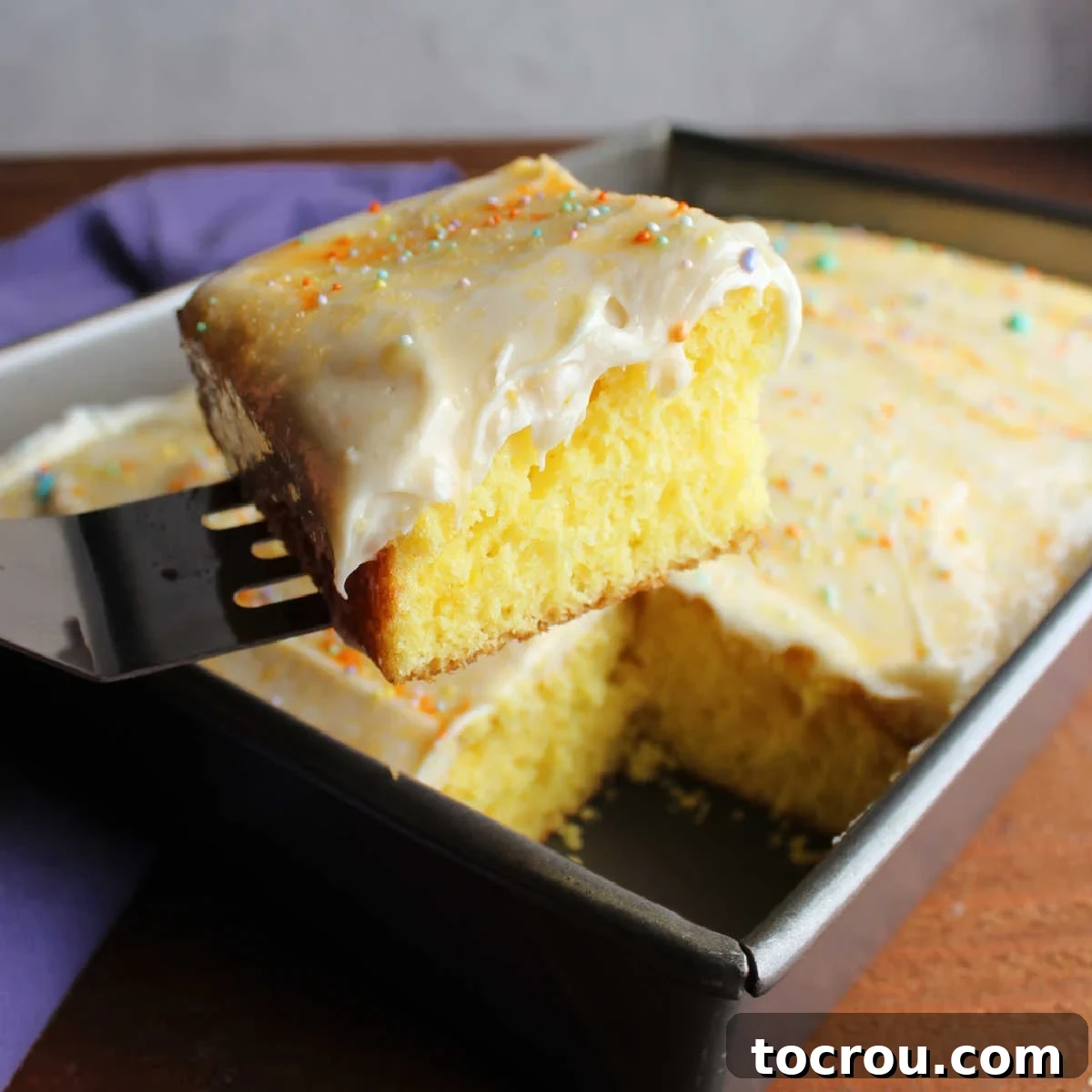 Spatula lifting out piece of lemon cake topped with lemon cream cheese frosting and sprinkles. 