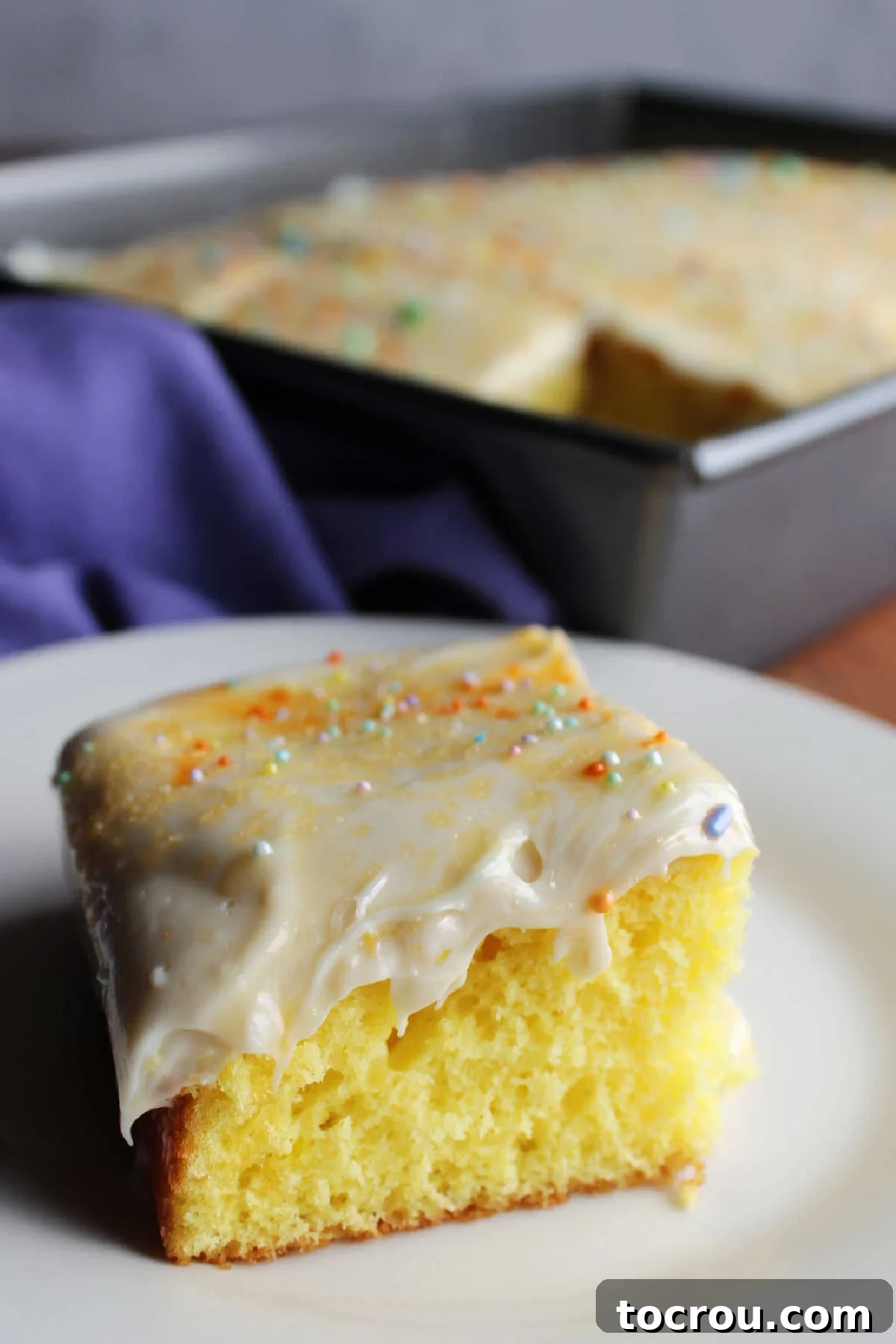 Close up of a piece of lemon cake topped with creamy lemon cream cheese frosting and colorful sprinkles. 