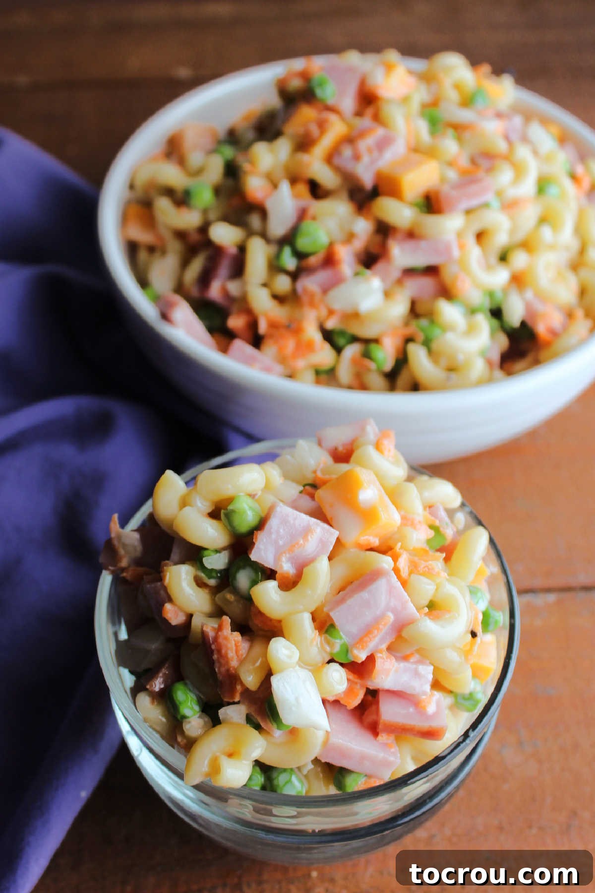 Small glass serving bowl filled with loaded sweet pasta salad with larger serving bowl in background.