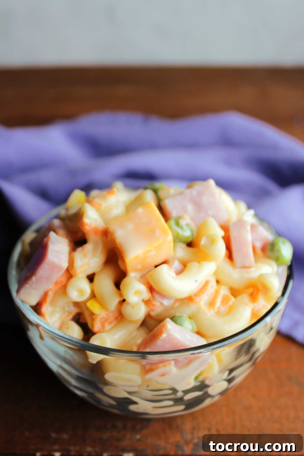 Small glass bowl filled with creamy sweet macaroni salad with cheese and ham.