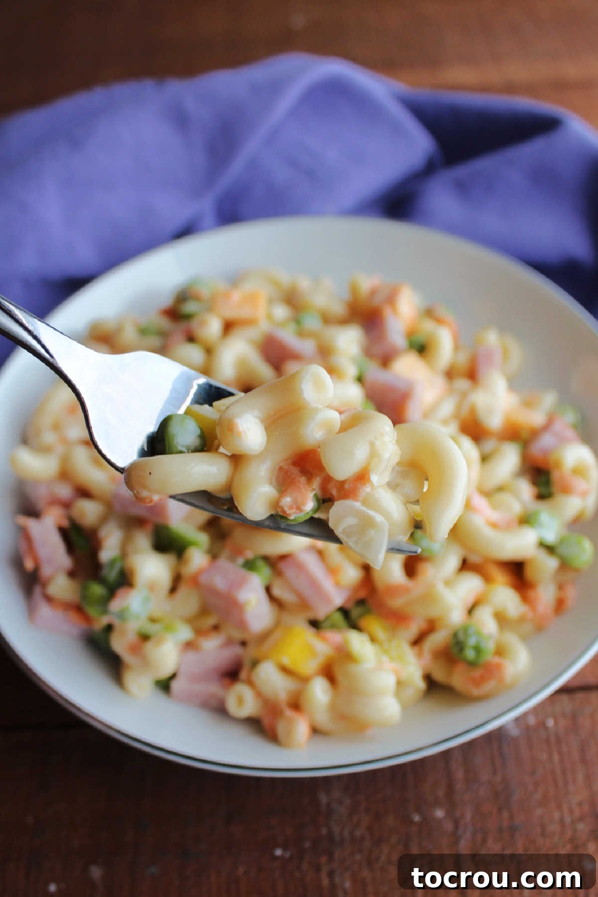 Bite of sweet macaroni salad on fork showing peas, onion, and shredded carrots.