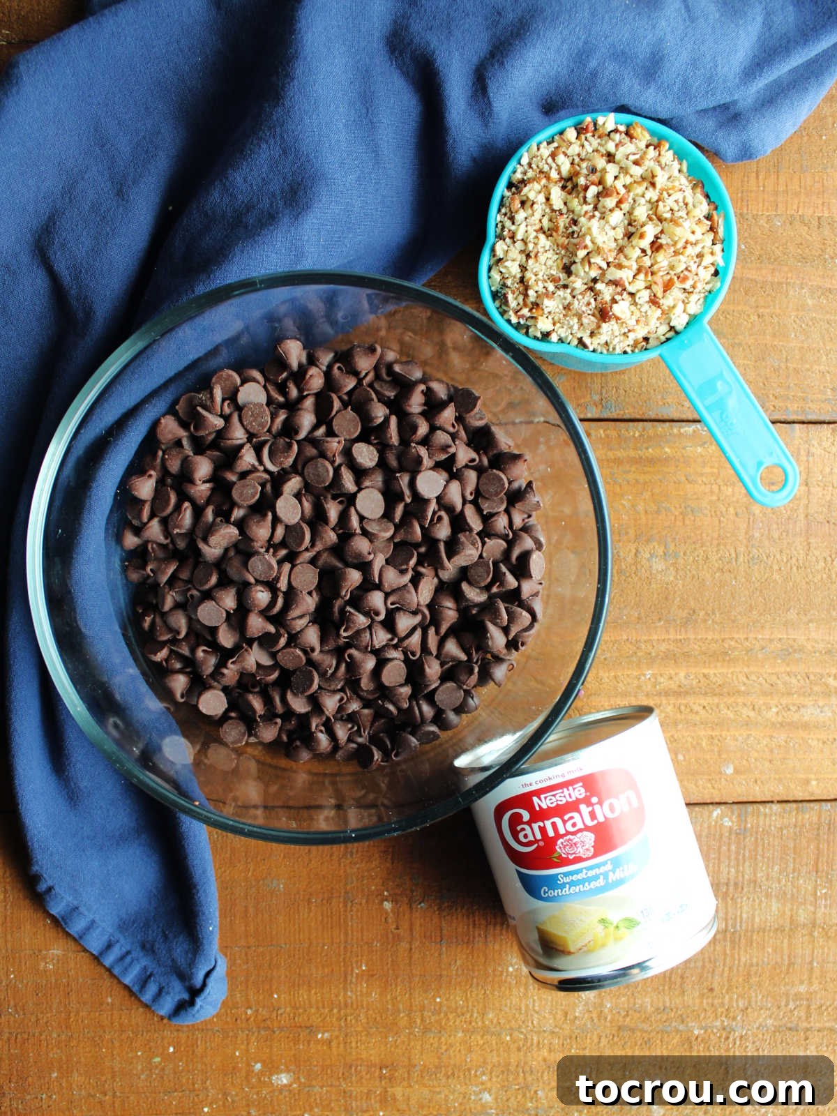 Key ingredients for fudgy chocolate ice cream cups, including glossy chocolate chips, a can of sweetened condensed milk, and a scattering of finely chopped pecans, neatly arranged and ready for preparation.