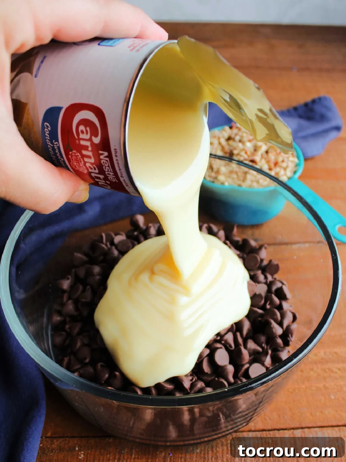 A steady stream of creamy condensed milk being poured over a bowl of rich chocolate chips, illustrating the start of the simple melting process for the fudge cups.