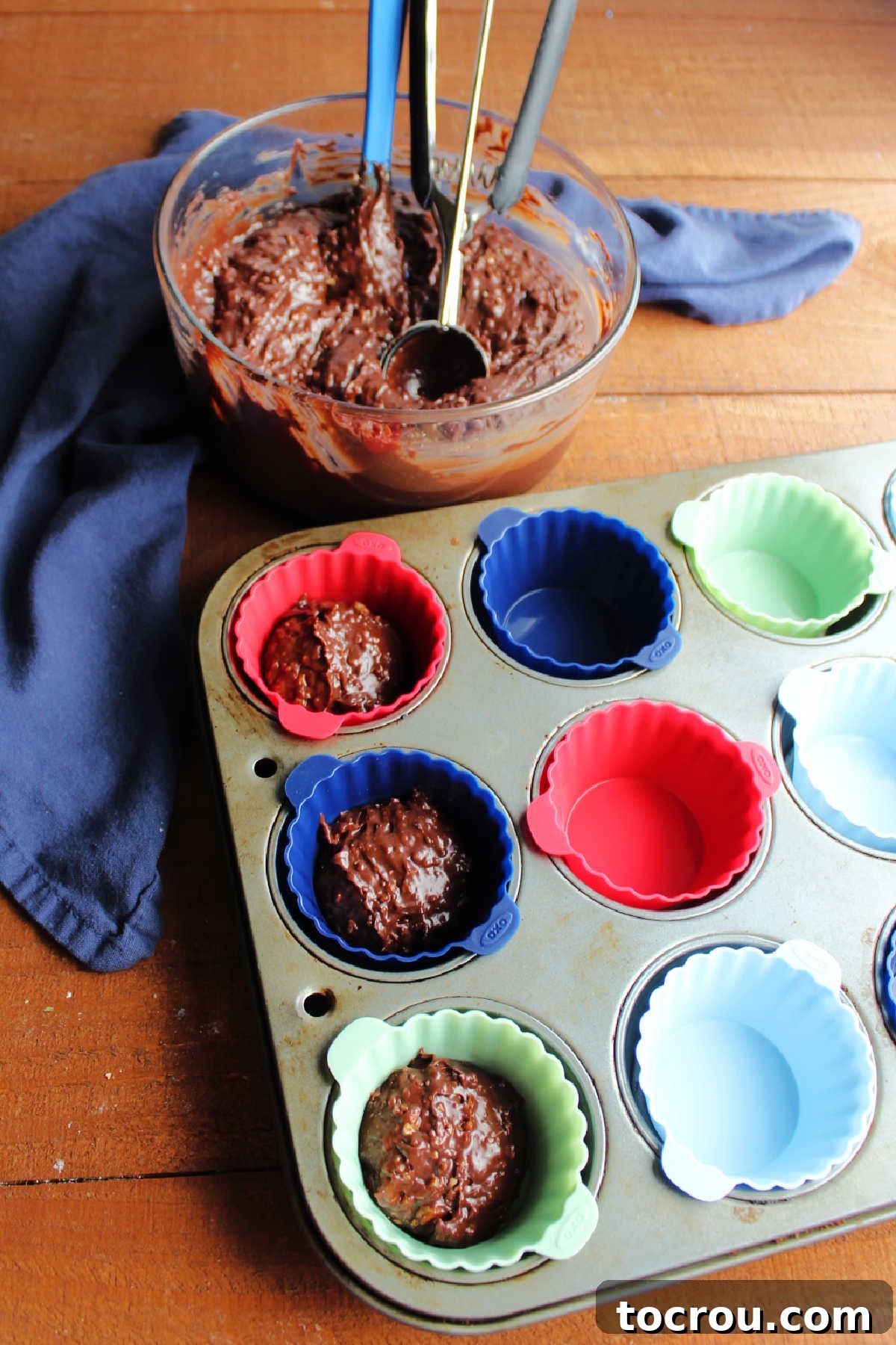 A medium cookie scoop expertly places a portion of the melted pecan fudge mixture into a cupcake liner, ensuring consistent sizing for each ice cream cup.