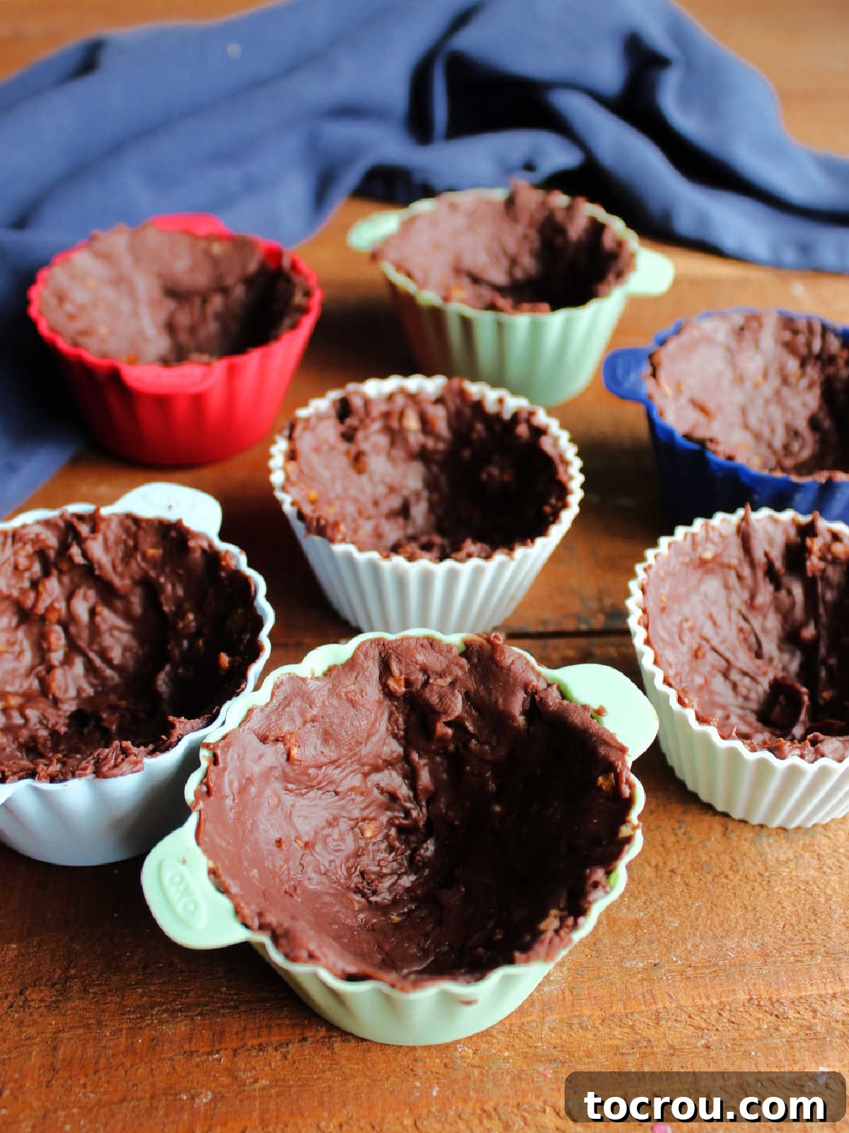 A tray of frozen fudge ice cream cups rests in their silicone cupcake liners, perfectly chilled and firm, ready for the next step of deliciousness.