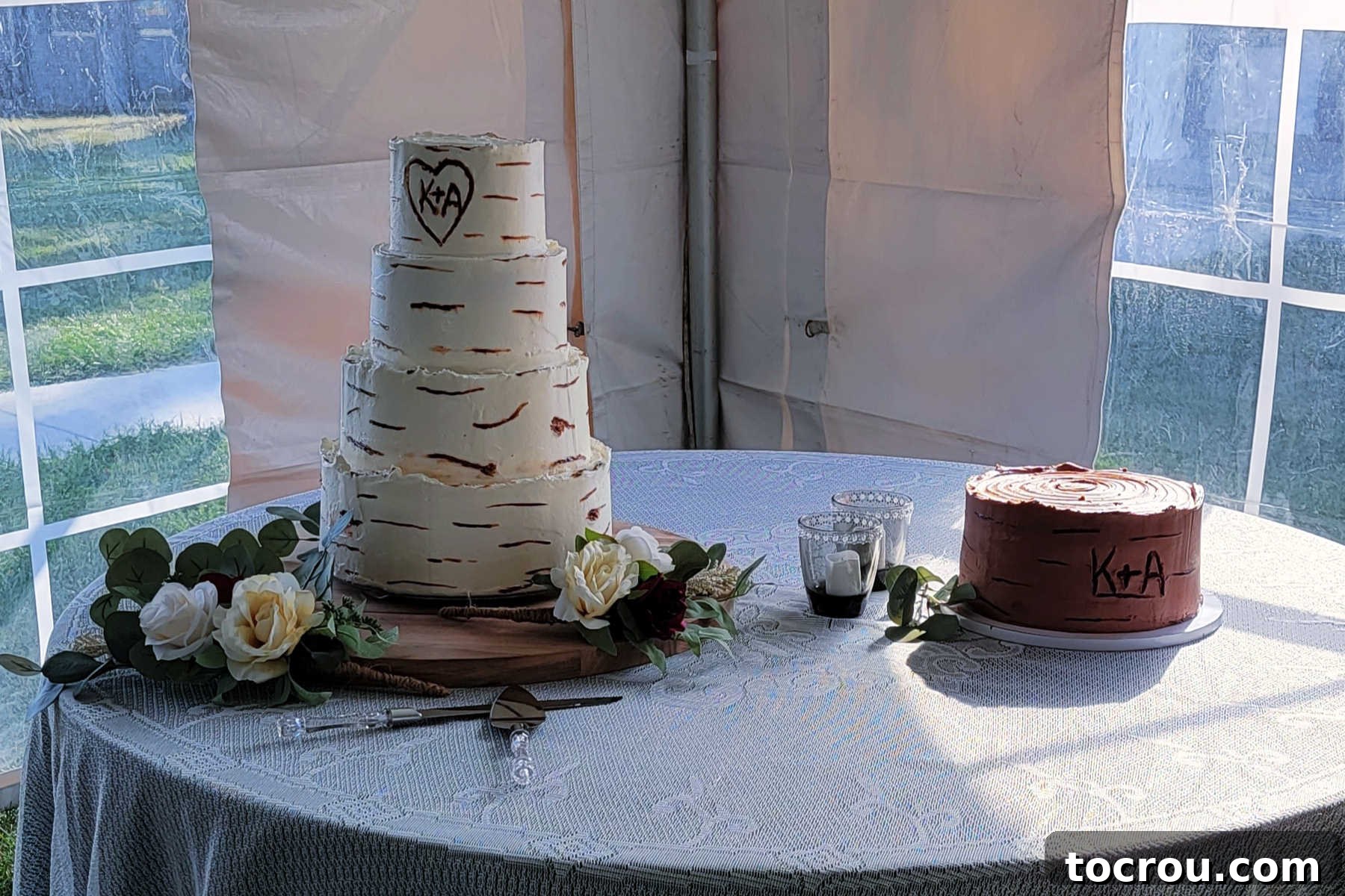 The 10-Inch Vanilla Classic 6 Wedding cake table with 4 tier vanilla cake with birch tree bark looking finish and carved in initials next to a 10 inch chocolate groom's cake with similar birch look and carved initials.