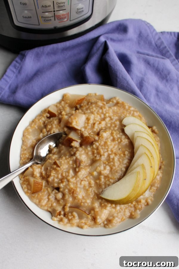 Garnished Steel Cut Oats Close-up of a bowl of steel cut oatmeal with slices of fresh pear on top, and an Instant Pot in the soft-focus background.