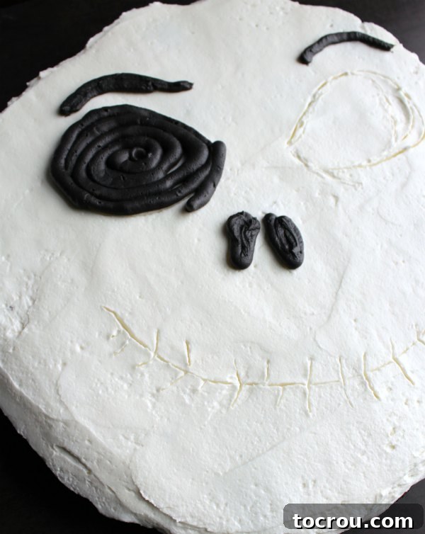 piping black frosting over traced lines on cupcake cake to start making the face details