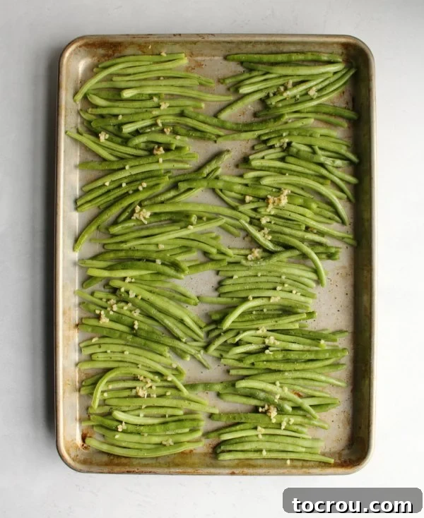 Fresh green beans and minced garlic spread on a baking sheet, prepped for roasting.