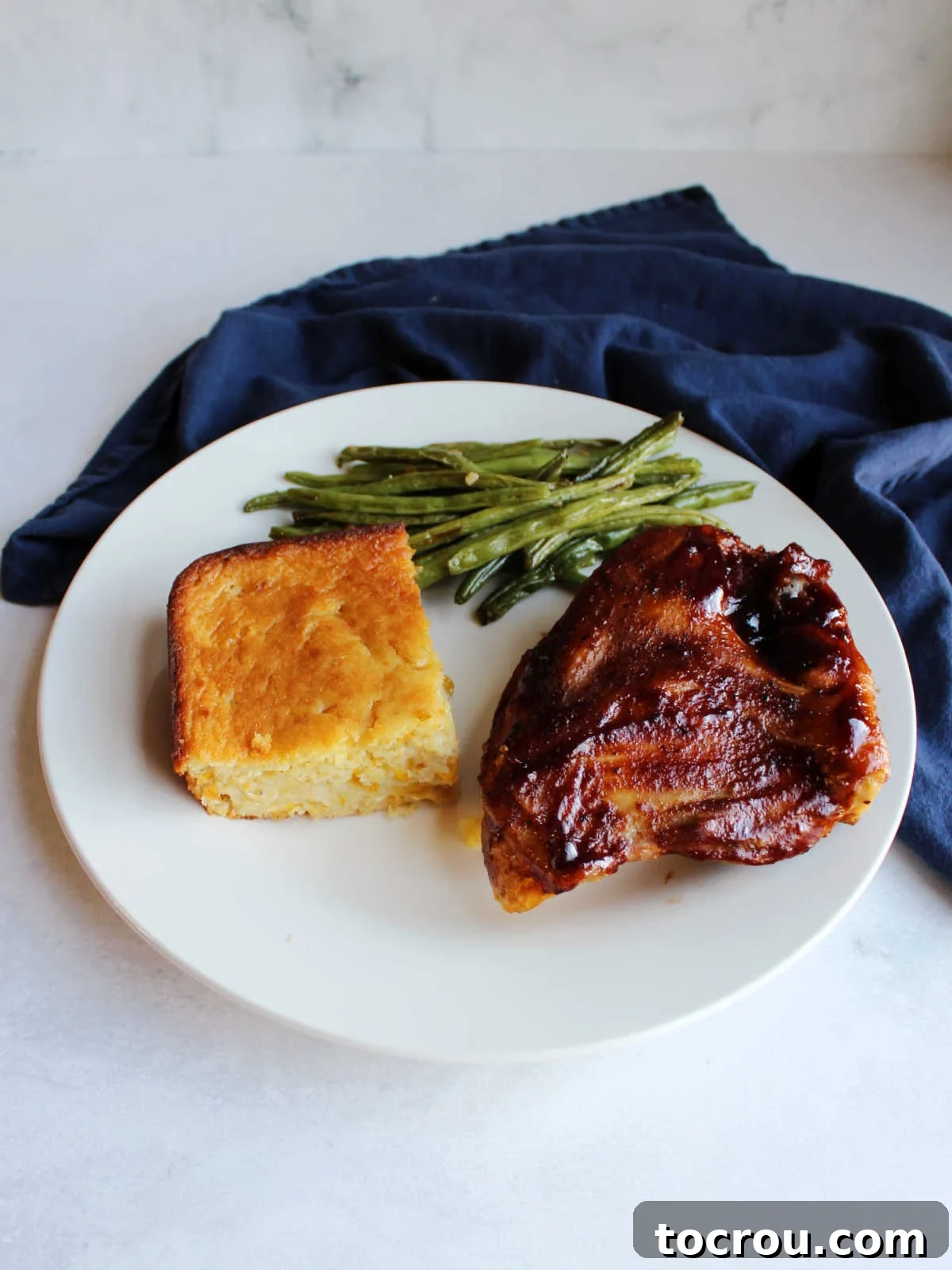 Complete Oven Baked BBQ Chicken Dinner square piece of corn pudding on plate with bbq chicken and green beans ready to eat.