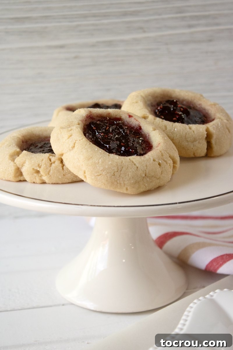 Jelly-Kissed Peanut Butter Bites 3 Small cake stand with an array of golden-brown peanut butter thumbprint cookies, some filled with jam.