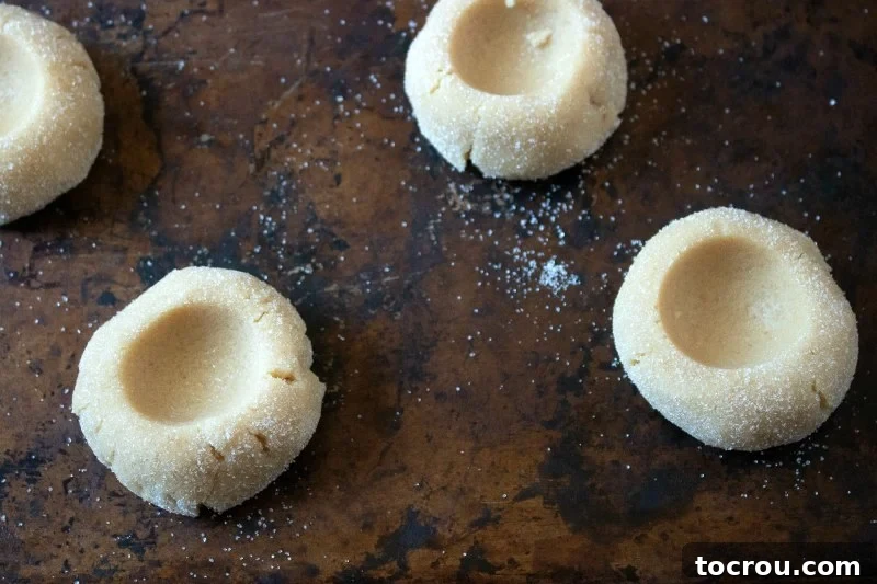 Jelly-Kissed Peanut Butter Bites 6 Rows of peanut butter cookie dough balls, lightly coated in sugar, each with a thumbprint indent in the center.