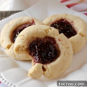 plate with three peanut butter and jelly thumbprint cookies, one with a bite taken out.