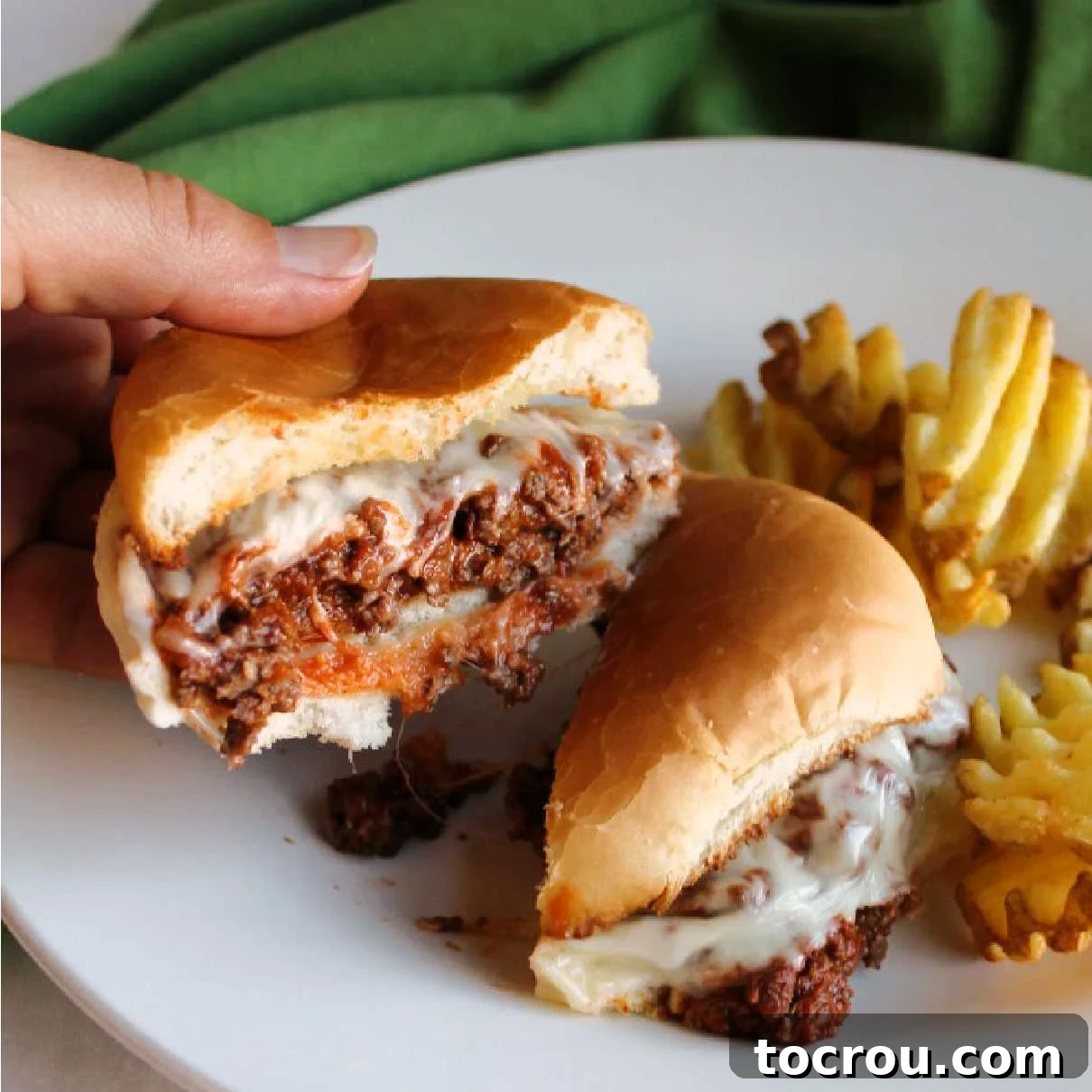 A freshly cooked pizza burger, cut in half, revealing its melted cheese and saucy meat filling. One half is held up, showcasing the enticing layers.