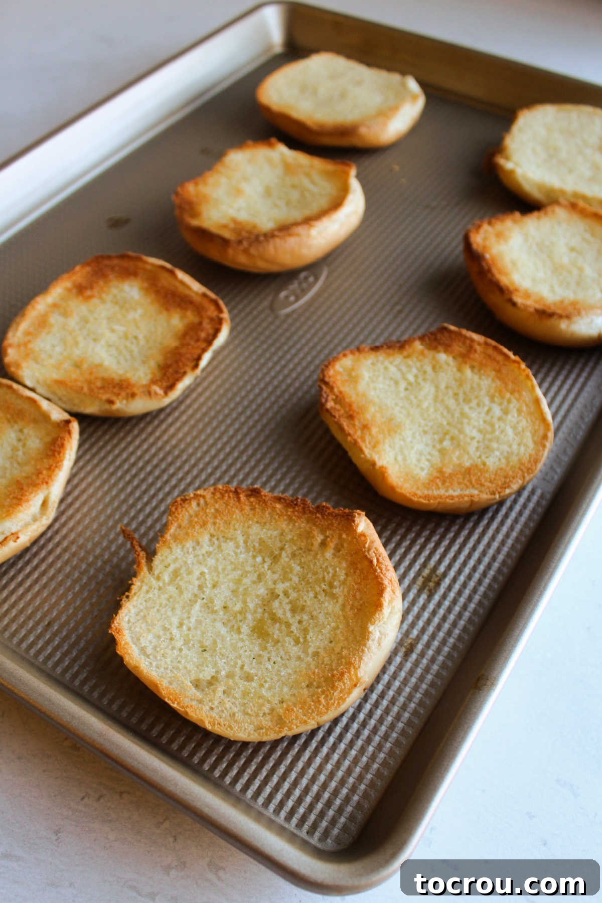 Toasted hamburger buns, glistening with garlic butter, arranged on a baking sheet, ready for the pizza burger toppings.