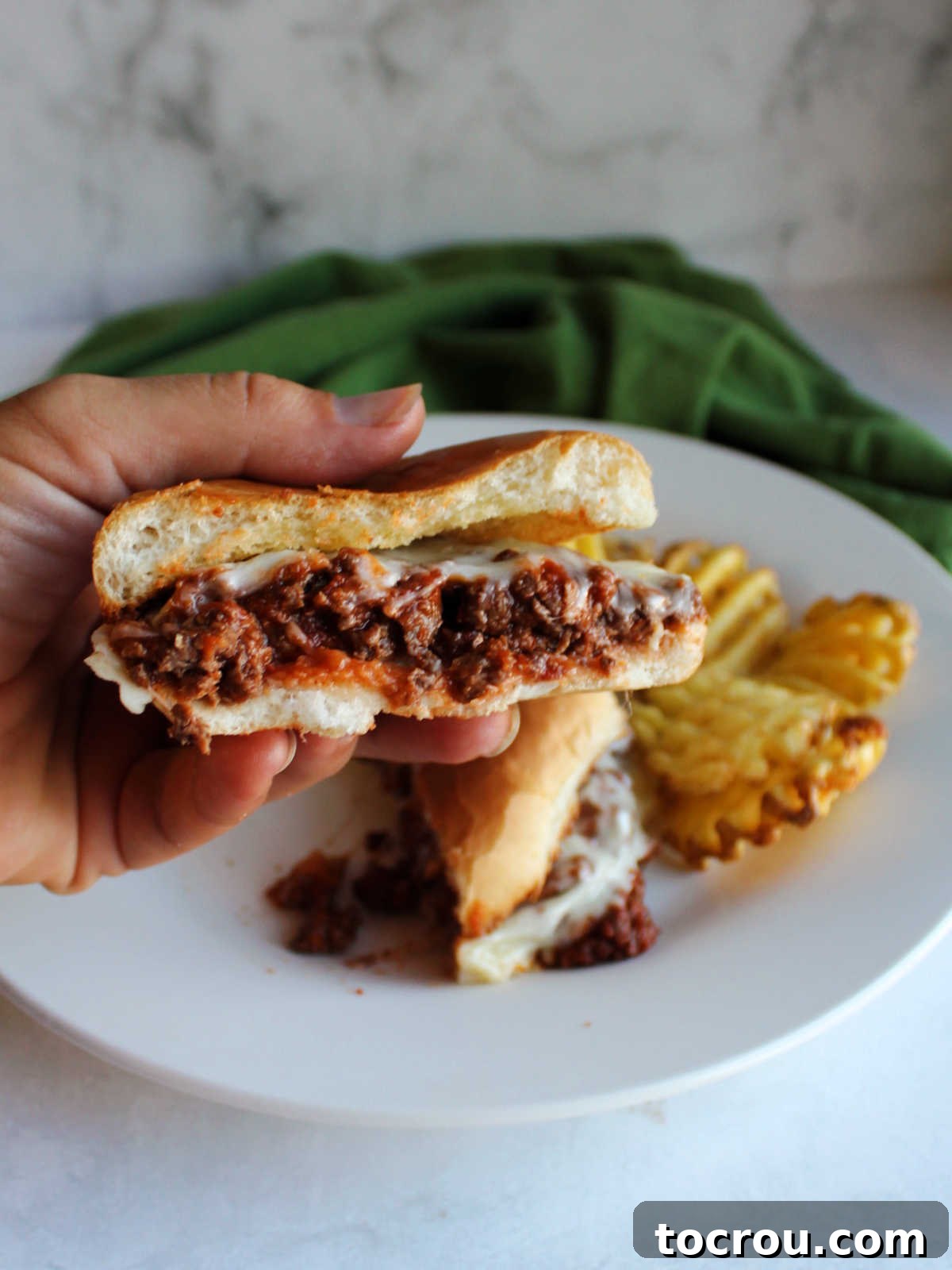 A hand holding up half of a pizza burger, clearly showing the loose, saucy meat filling and the beautifully melted mozzarella cheese inside.