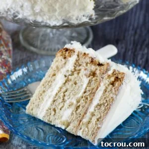 Wedge of 4 layer banana cake with fluffy white frosting and coconut on blue plate, ready to eat.