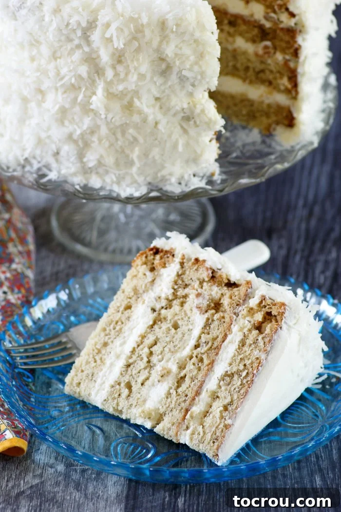 Slice of Maida Heatter's star spangled cake with 4 layers of banana cake, a fluffy white frosting and a coating of coconut around the edges.