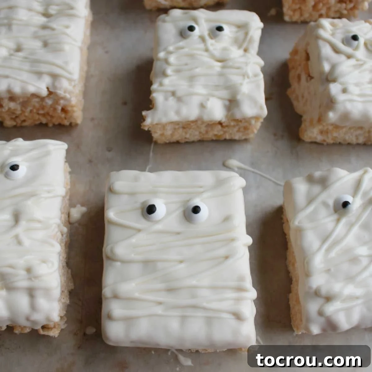 Rice krispie treats decorated with white chocolate and candy eyeballs to look like mummies, presented on a festive Halloween platter.