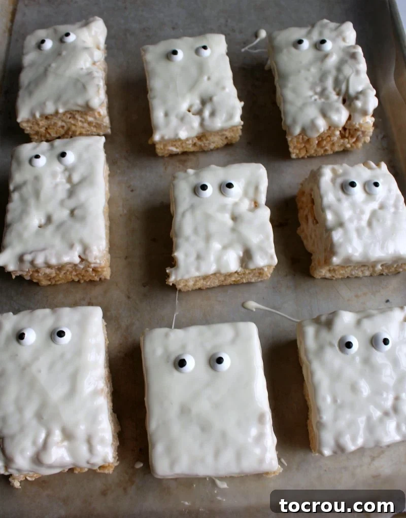 A tray filled with white chocolate-dipped rice crispy treats, each topped with two candy eyeballs, resembling cute ghosts.