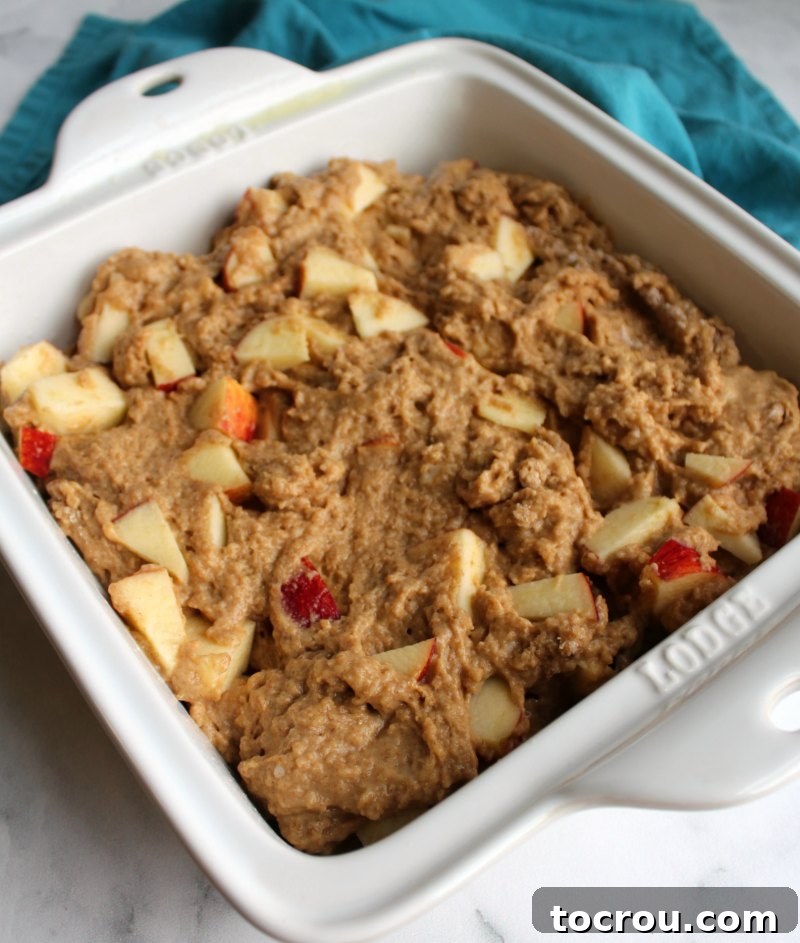 Thick, rich rustic buttermilk apple cake batter smoothly spread into an 8-inch square baking dish, ready for the oven.