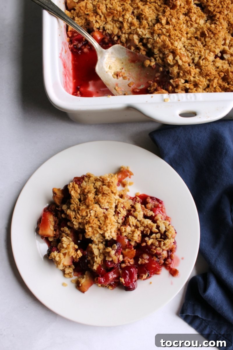 Small plate with serving of cranberry apple crisp with pan and antique berry spoon in the background.