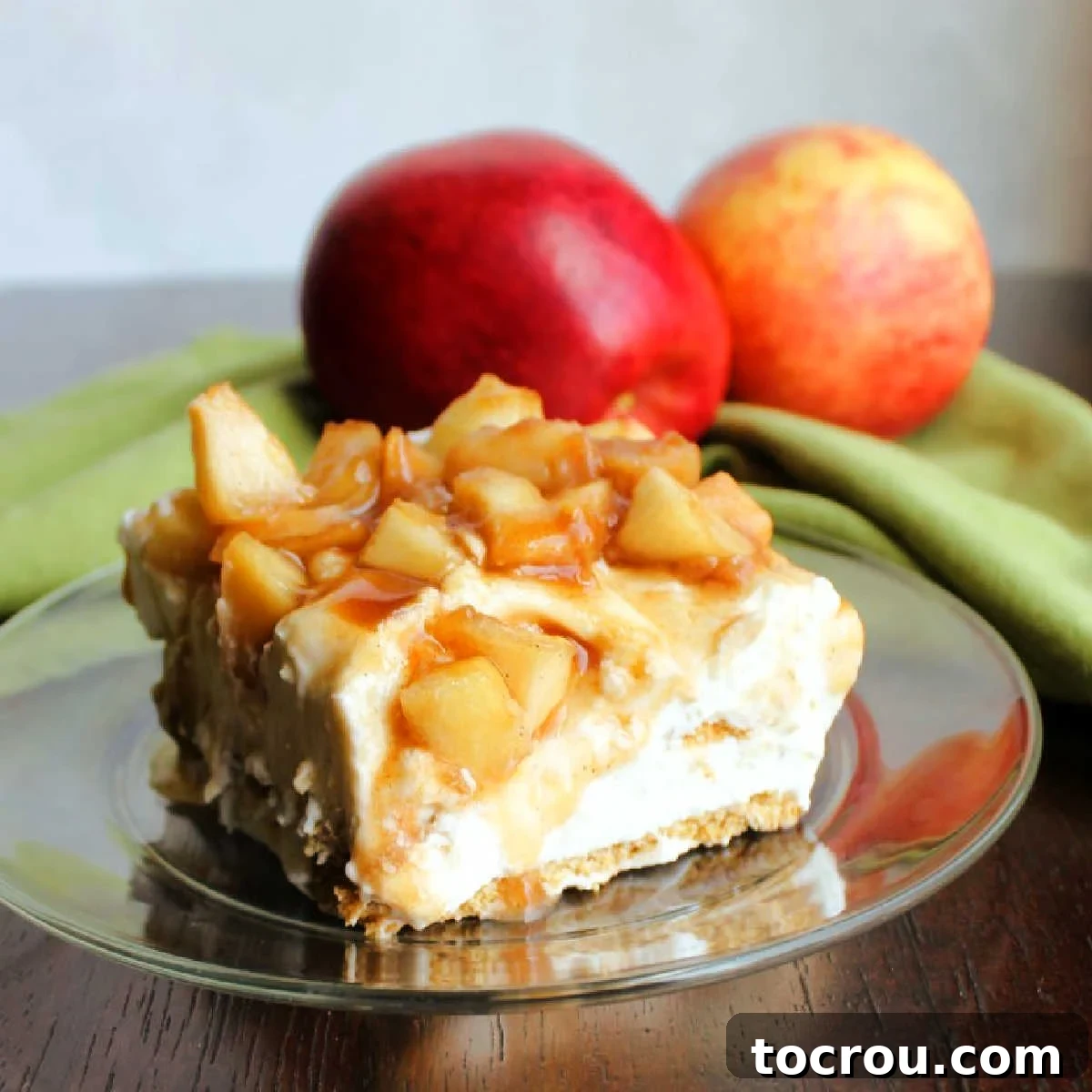 No bake creamy caramel apple icebox cake is a perfect way to transition to fall flavors without heating up the house. The vanilla cream cheese filling, Graham crackers and cinnamon brown sugar apples come together to make the perfect slice of dessert. close up slice of icebox cake with layers of graham crackers, fluffy cream cheese filling and cinnamon spiced caramelized apples with apples in the background.