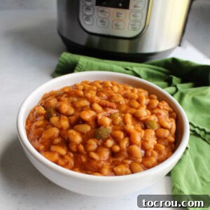 Serving bowl filled with homemade maple bacon baked beans in front of the Instant Pot they were cooked in.