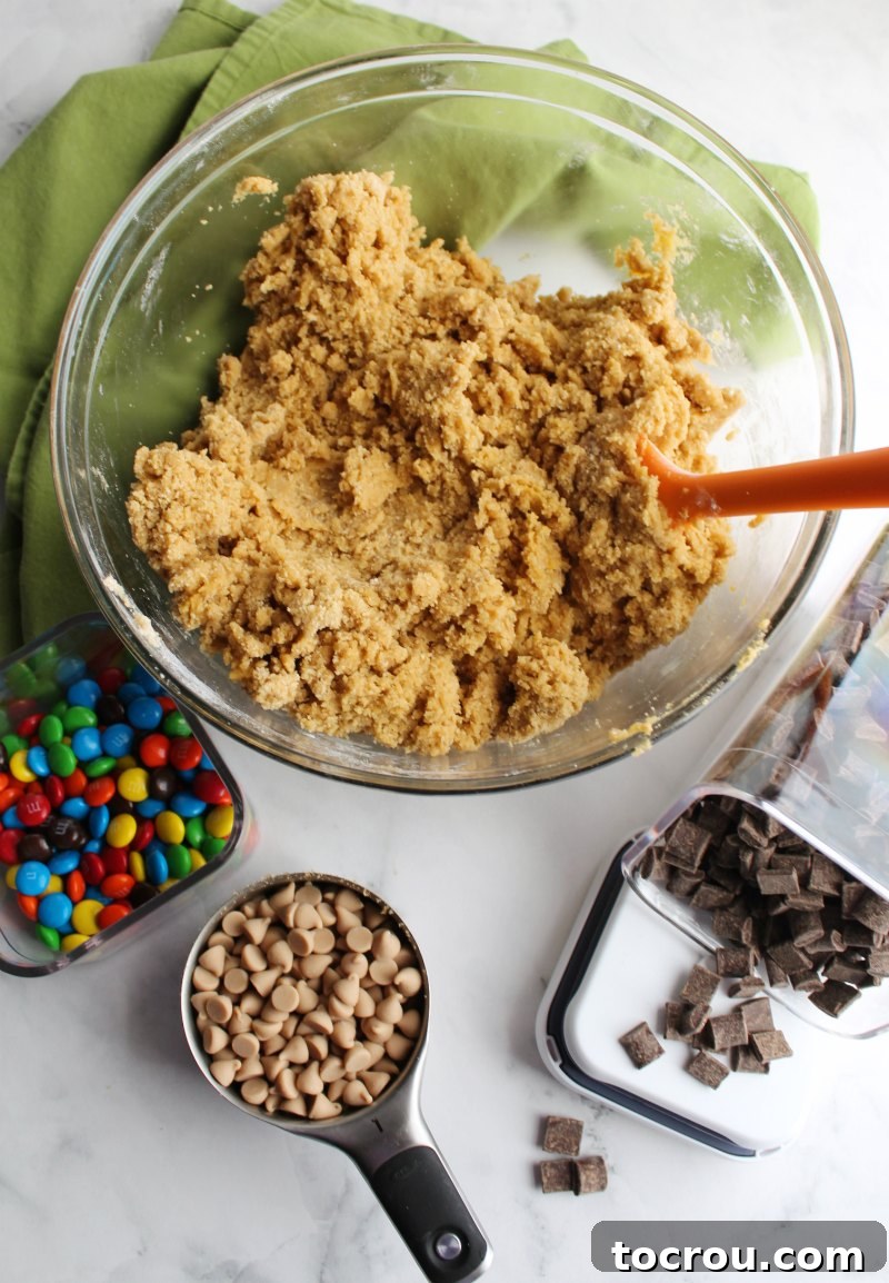 Irresistible Chewy Salted Caramel M and M Blondies 2 mixing bowl of blondie dough with container of chocolate chunks, m&ms and salted caramel chips in measuring cup.