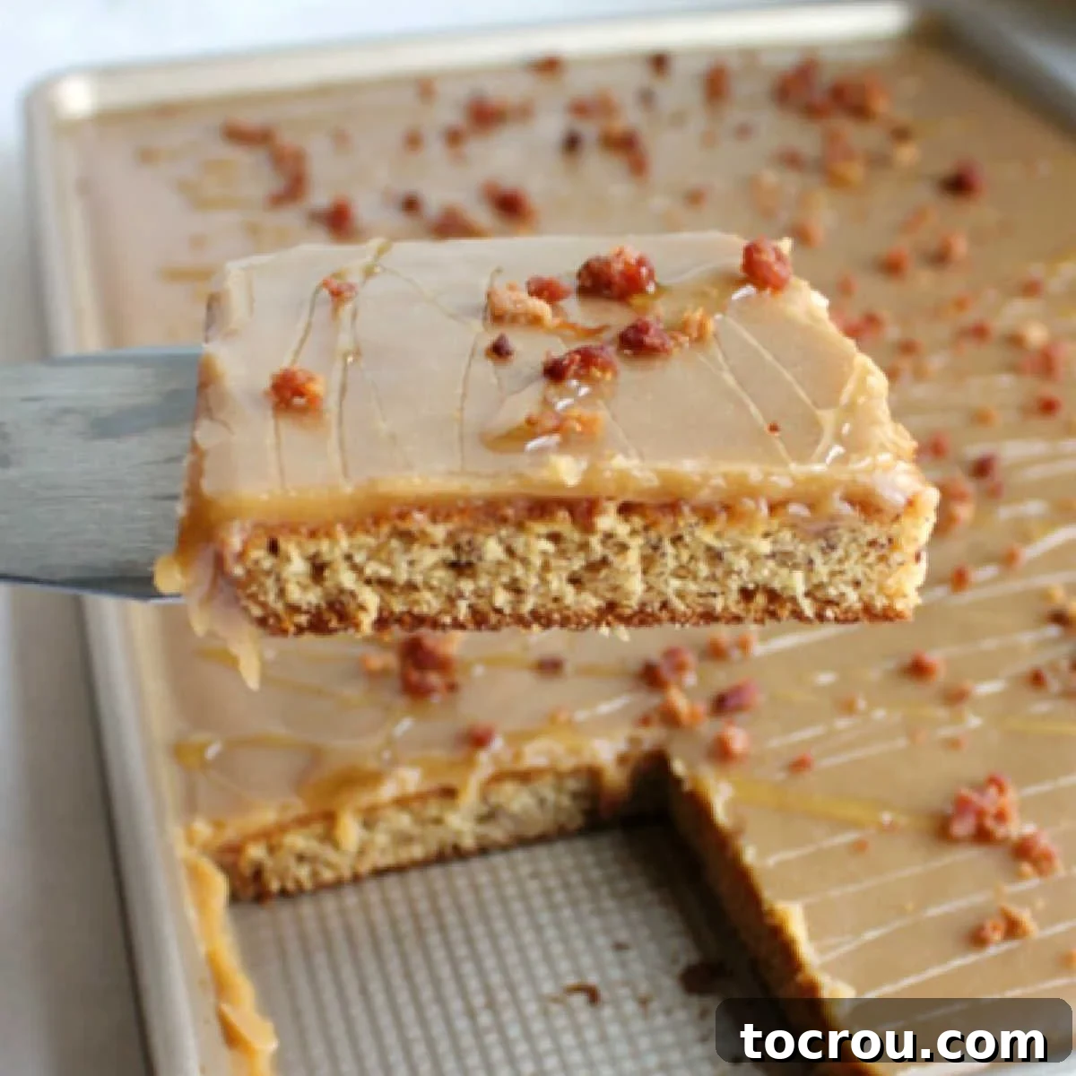 Close-up shot of the first slice of Elvis sheet cake being lifted from the pan, revealing the moist banana cake, smooth peanut butter icing, and crumbles of cooked bacon.