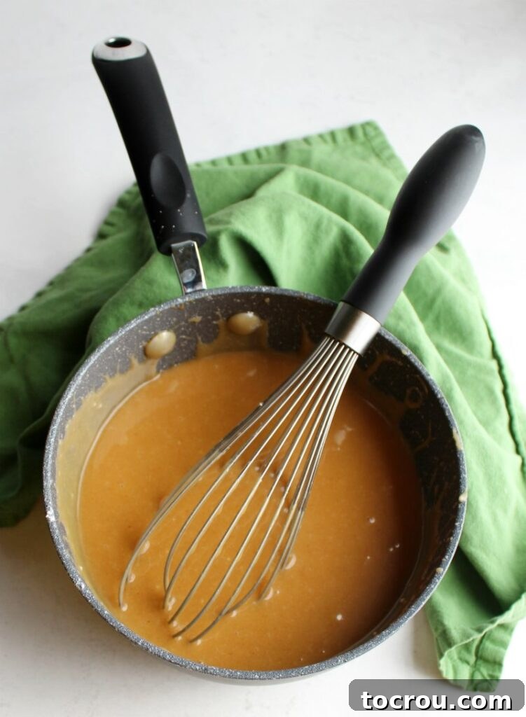 Peanut butter icing in a saucepan with a whisk, showing its smooth consistency and readiness for the cake.