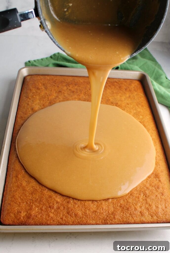 Pouring smooth peanut butter icing generously over a warm banana sheet cake, ensuring full coverage.